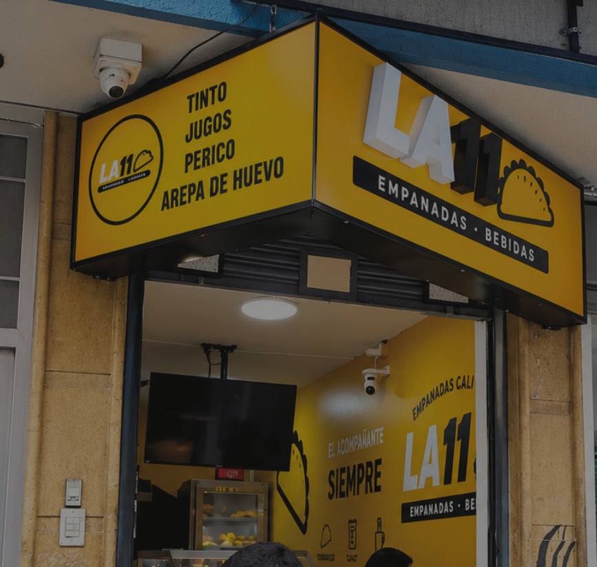 Fachada amarilla de un local de empanadas con aviso luminoso y vinilo mural